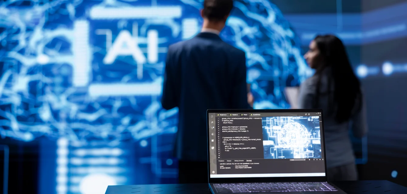 focus-on-laptop-running-ai-cognitive-computing Laptop displaying AI cognitive computing technology, with IT staff members working in the blurry background, highlighting the use of advanced AI tools for cybersecurity