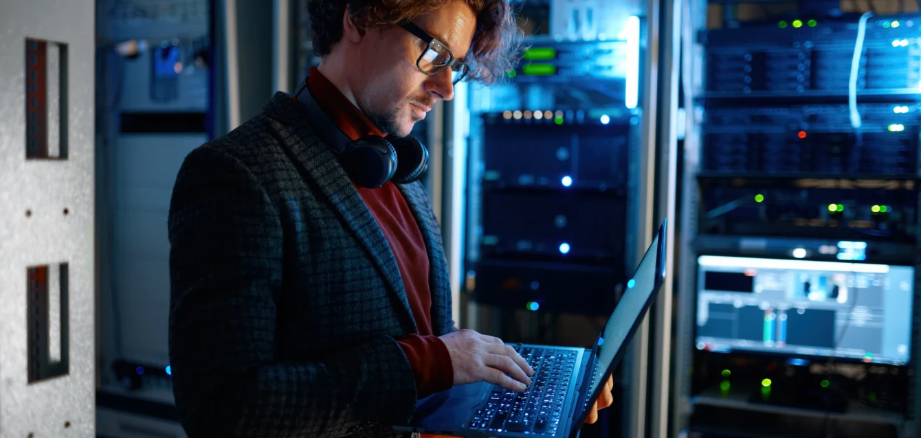 it-technician-checking-the-servers-vitals-using-laptop IT technician examining server diagnostics on a laptop in a dark server room, highlighting the importance of addressing cybersecurity gaps often overlooked by SMEs